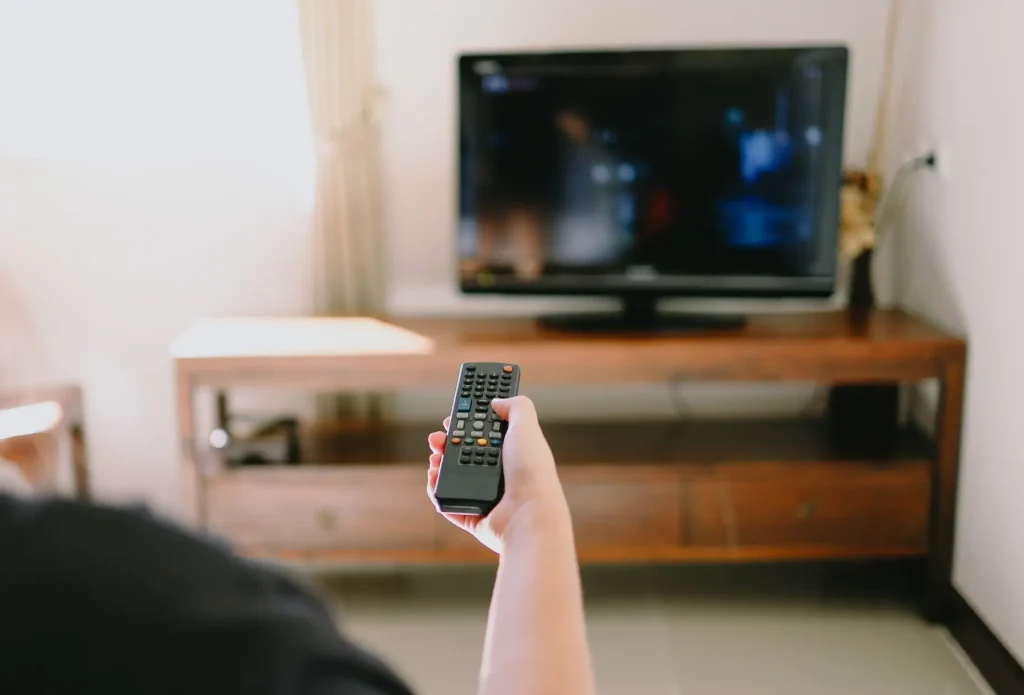 奥にテレビ、それに向けてリモコンを向ける手